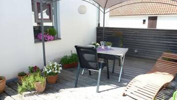 A patio with a table and chairs, surrounded by potted plants and a wooden deck.