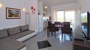 Un salon moderne comprenant un canapé, une table à manger, des chaises, un téléviseur et un coin cuisine avec un réfrigérateur et une cuisinière.
