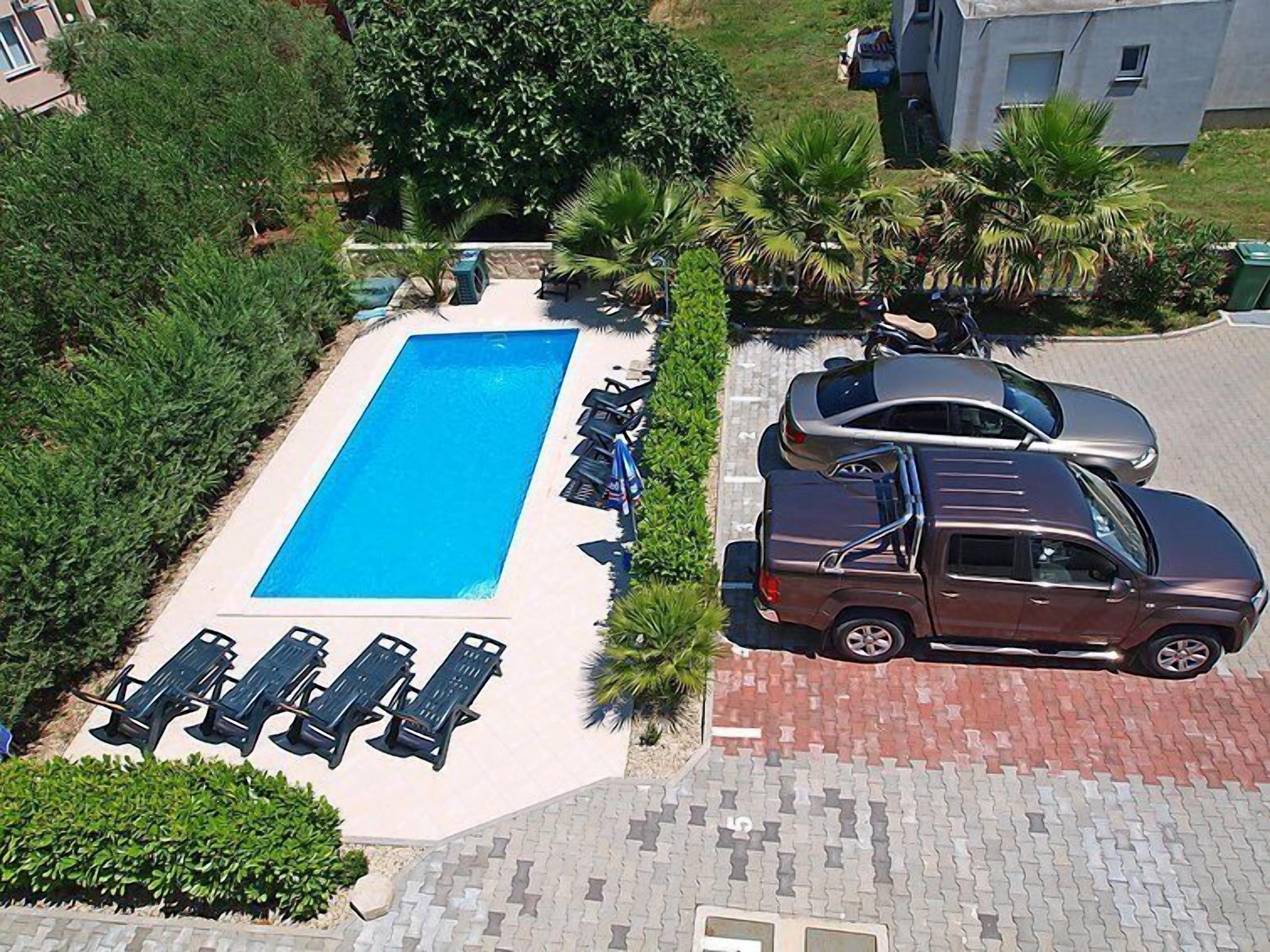 An aerial view of a swimming pool with lounge chairs and a parked car.
