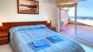 Une chambre à coucher avec un lit, une table de chevet, une lampe, un tableau et une vue sur la plage.