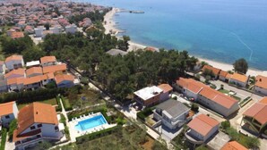Vista aérea de uma área residencial à beira-mar, com casas, praia e piscina.