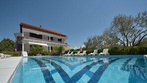 Piscina com padrão de azulejos, cercada por espreguiçadeiras e um edifício com telhado vermelho.