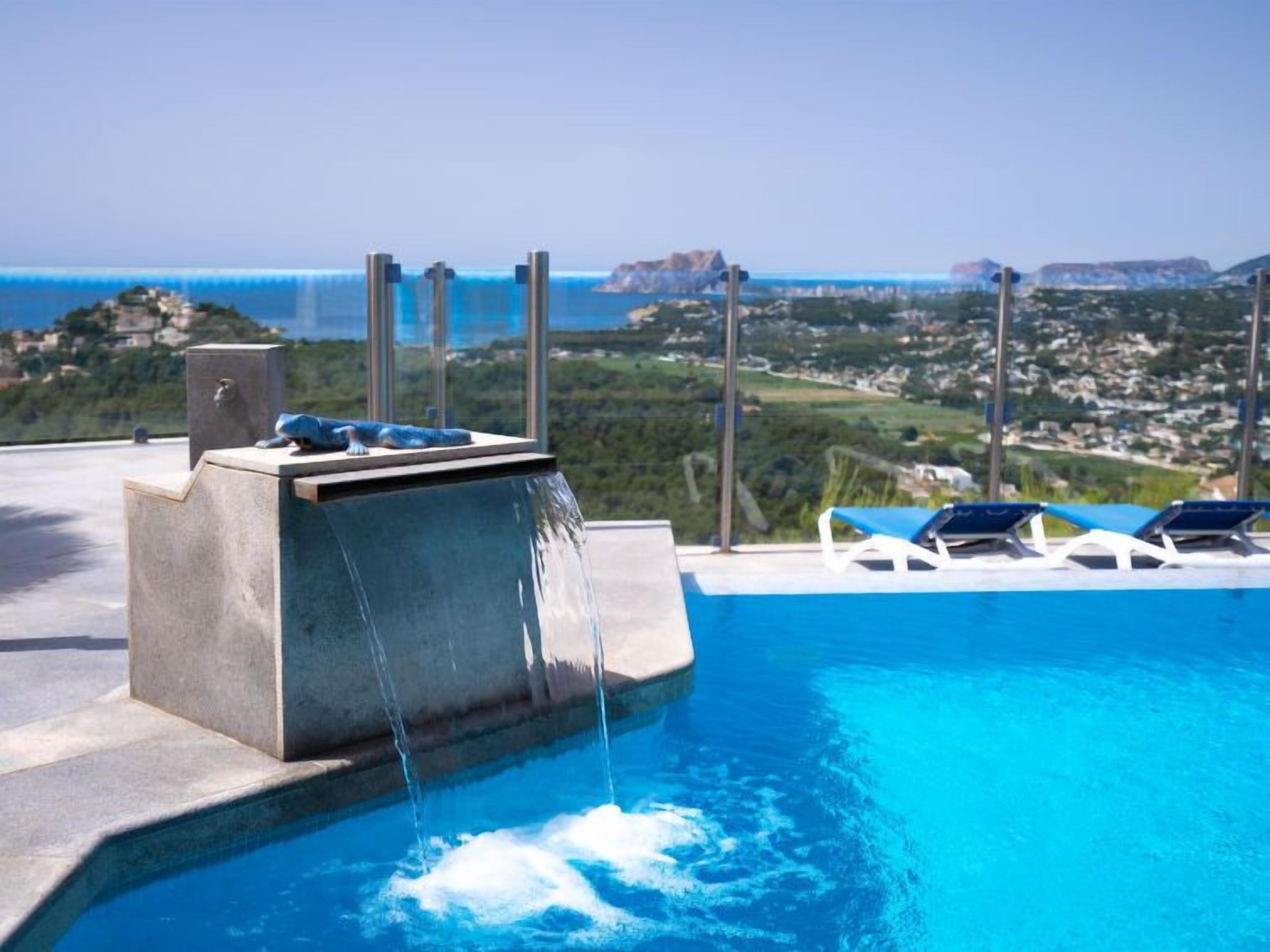 A pool with a waterfall feature, lounge chairs, and a view of a coastal landscape.