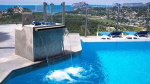 A pool with a waterfall feature, lounge chairs, and a view of a coastal landscape. - Finca Edel by Interhome (Moraira)