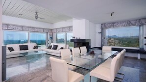 A spacious living room with a glass dining table, white sofas, and large windows offering a view of the landscape. - Finca Edel by Interhome (Moraira)