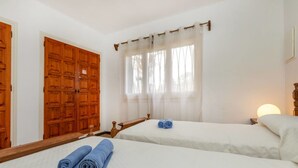Una habitación con dos camas individuales, un armario de madera, un espejo grande y una ventana con cortinas translúcidas.
