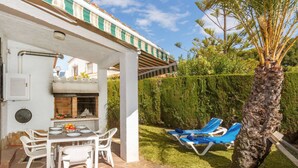 Un espacio de comedor al aire libre techado, con una parrilla, sillas blancas y una mesa lista para dos personas.