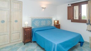 A bedroom with a bed, two bedside tables, a wardrobe, a window with curtains, and a wall-mounted light fixture.
