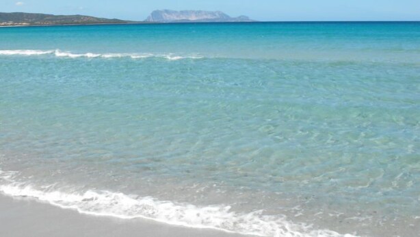 A beach with clear turquoise water and a distant mountain.