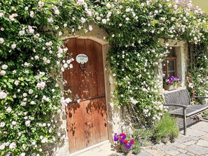 A rustic building with a wooden door, surrounded by lush climbing roses.