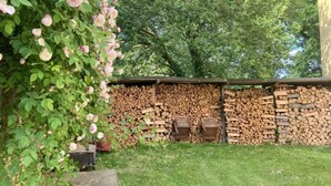 Un giardino con un roseto, una pila di legna da ardere e una panchina di legno.