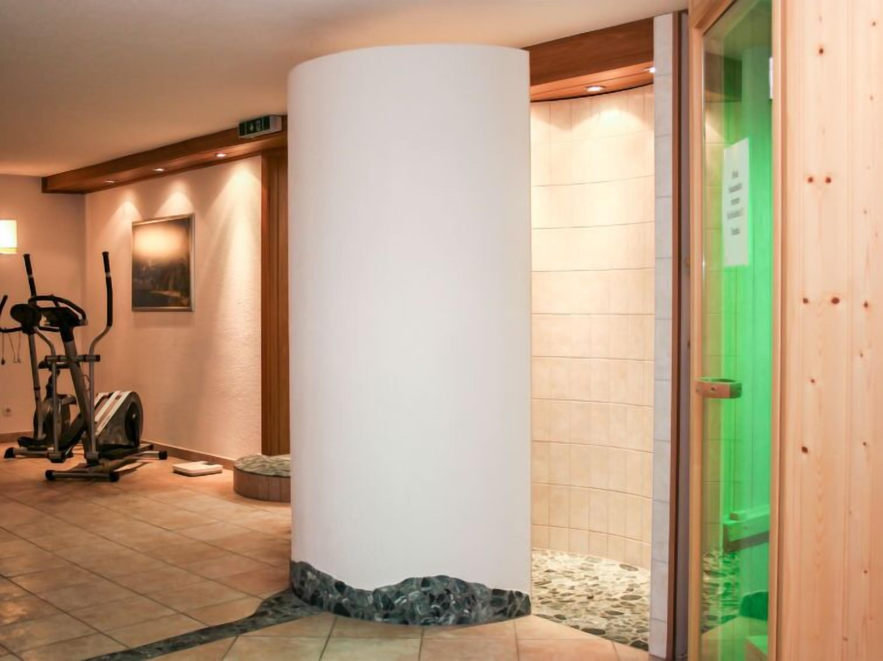 Uma área de spa com um grande pilar branco, equipamentos de exercício e uma porta verde.