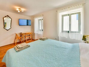 A bedroom with a bed, a desk, a chair, a TV, and two windows with curtains. - Vacation home Divna by Interhome (Selce)