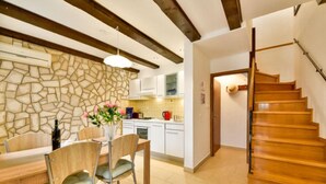Une cuisine moderne avec un mur de crédence en pierre, une table à manger en bois et des chaises. Un escalier mène à l’étage supérieur.