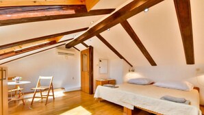 Une chambre avec un plafond en bois, un lit avec une literie blanche, une petite table avec des chaises et un appareil de climatisation.