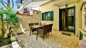 Une terrasse avec un sol en pierre, une table avec des chaises et une porte dotée d’un cadre vert.