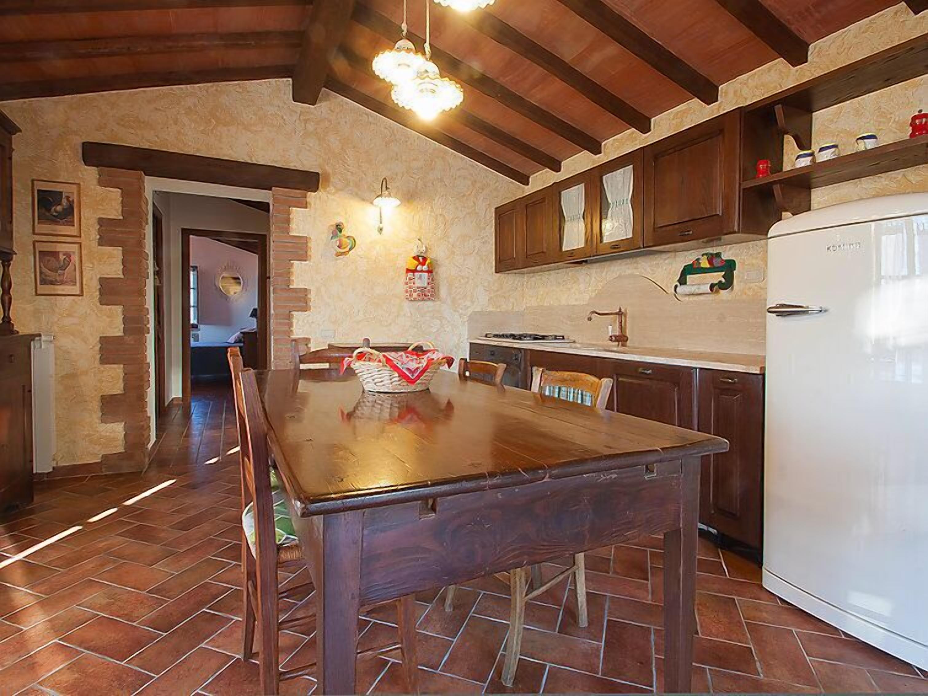 A kitchen with a wooden table, a white refrigerator, and a stone wall.