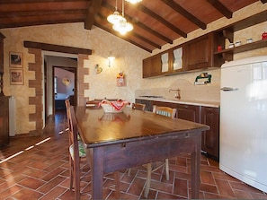 A kitchen with a wooden table, a white refrigerator, and a stone wall.