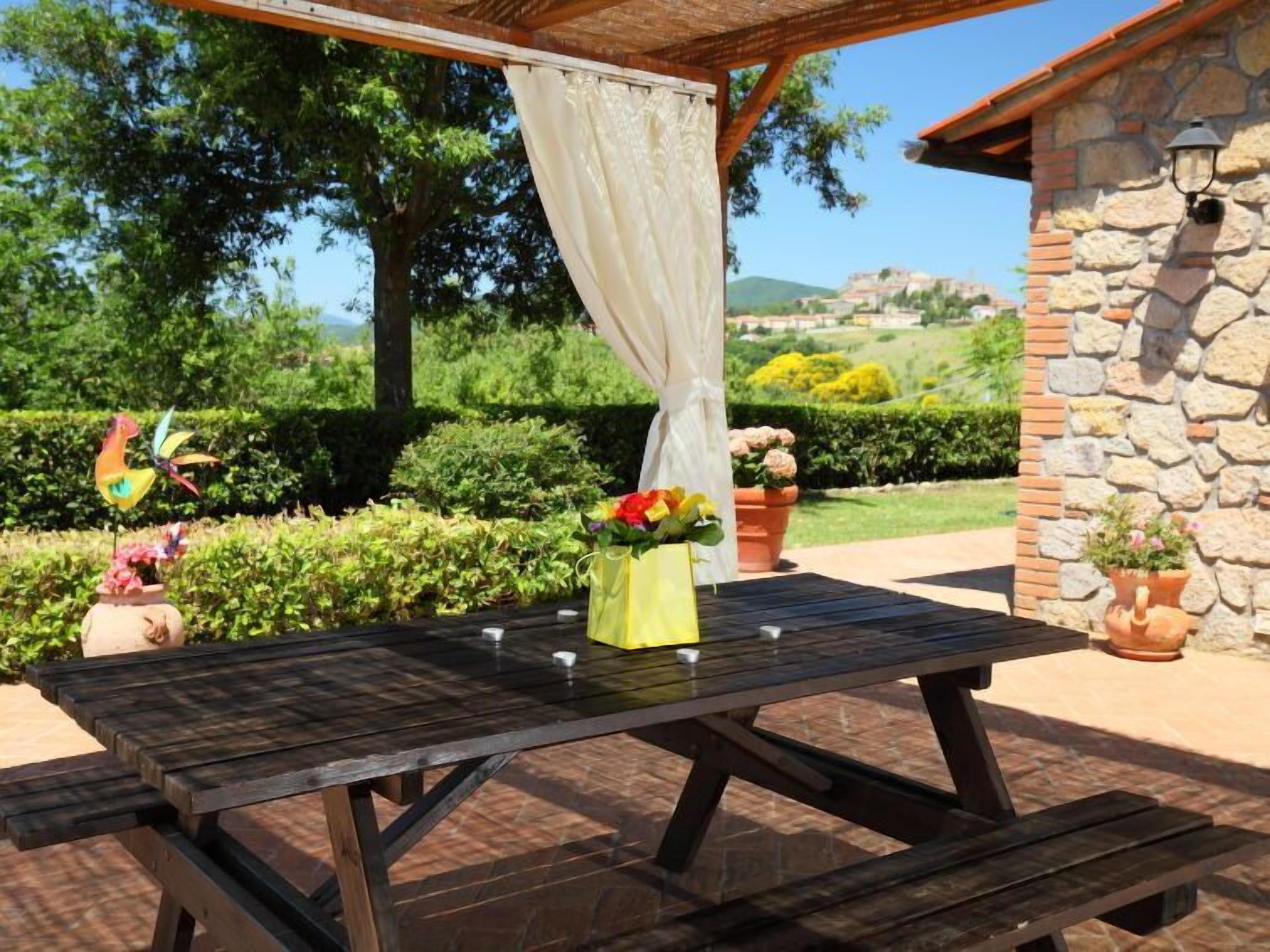 An outdoor patio with a wooden table, a white curtain, and potted plants.