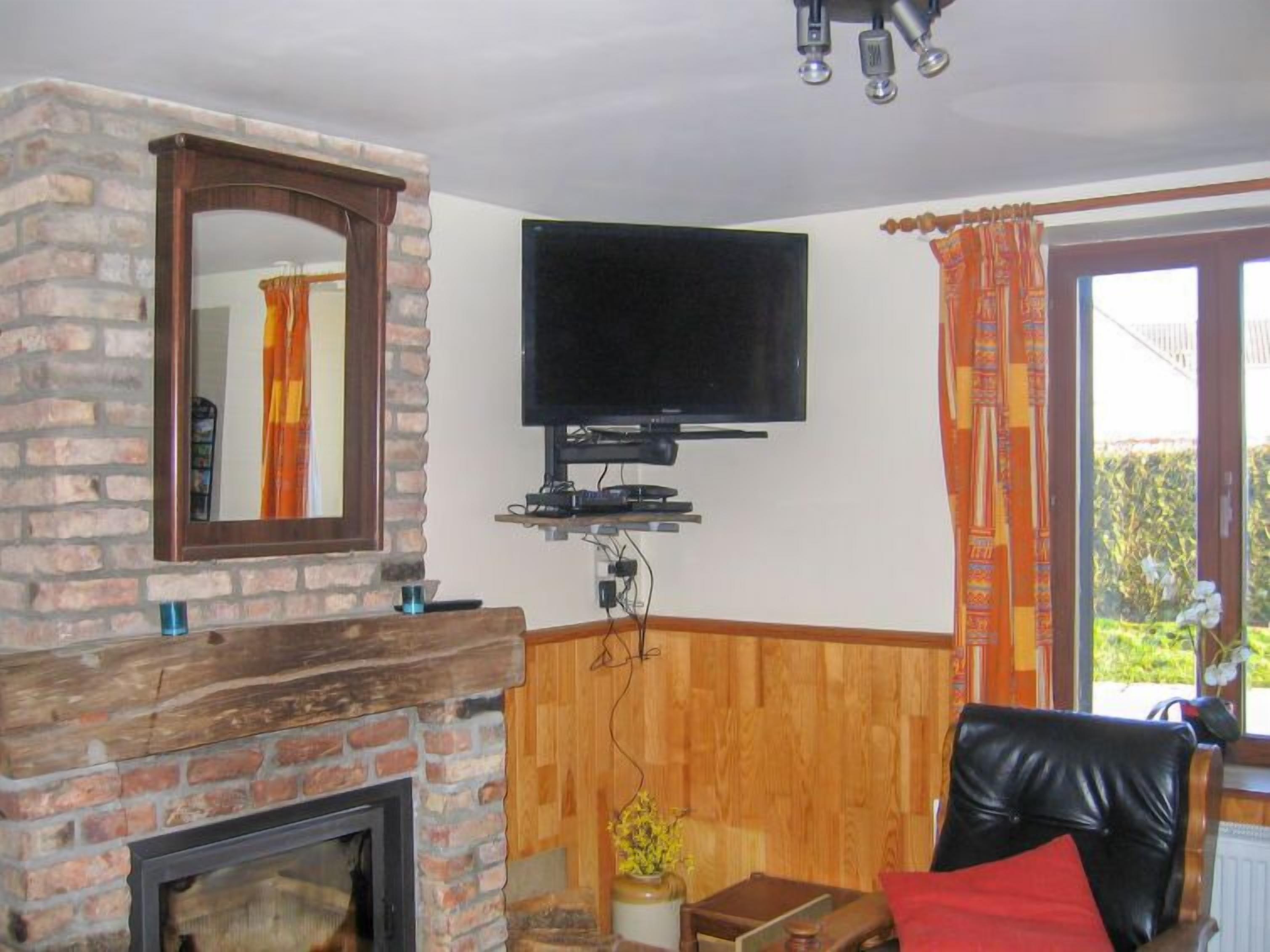 Un salón con chimenea de ladrillo, televisor montado y ventana con cortinas.