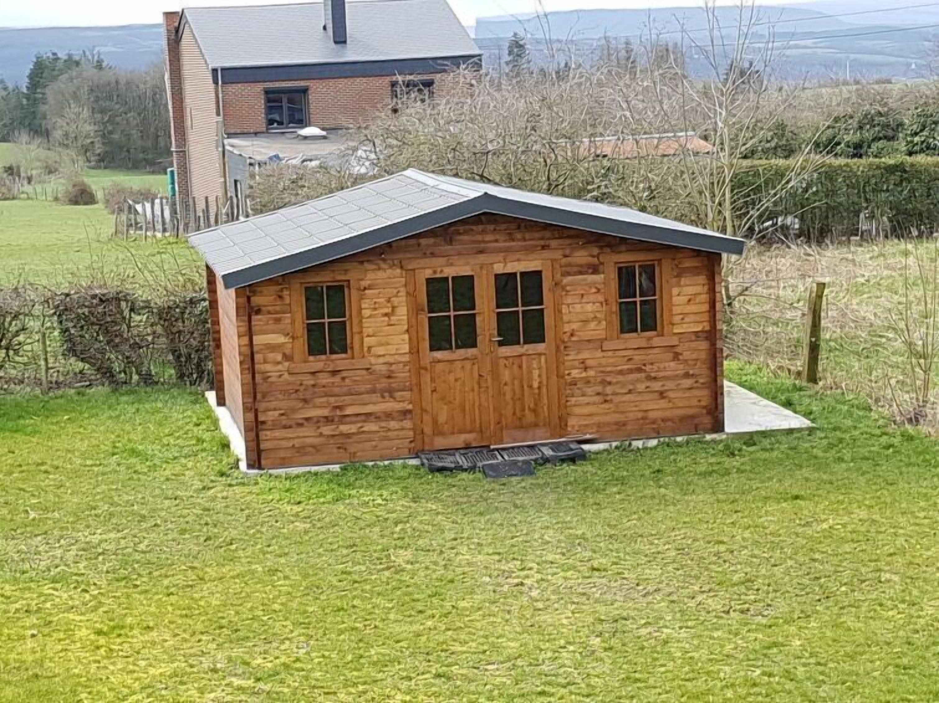 Una cabaña de madera pequeña con techo inclinado, una puerta principal y tres ventanas.