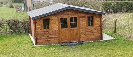 Una cabaña de madera pequeña con techo inclinado, una puerta principal y tres ventanas.