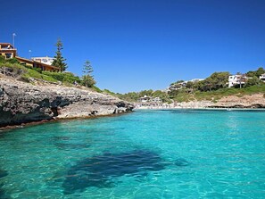 A coastal area with clear turquoise water, rocky shoreline, and buildings on the hillside. - Cala Mendia Sea Views by Interhome (Porto Cristo)