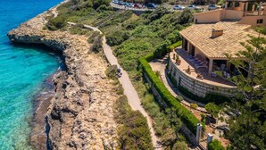 Una propietat a la costa amb un camí pavimentat que condueix a un edifici de teules, envoltada de vegetació i amb vistes al mar.