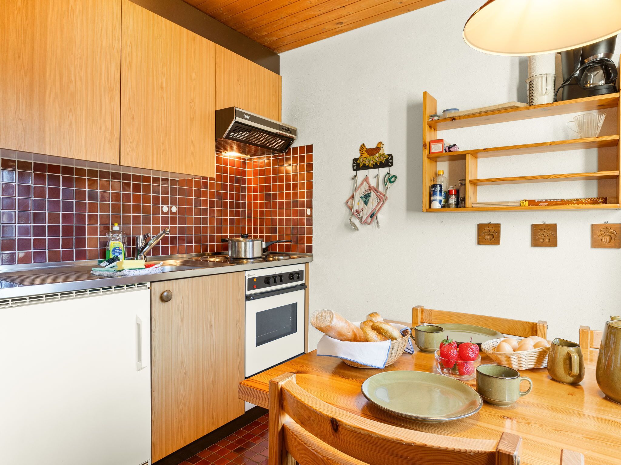 A compact kitchen with wooden cabinets, a tiled backsplash, and a dining area with a wooden table set for breakfast.