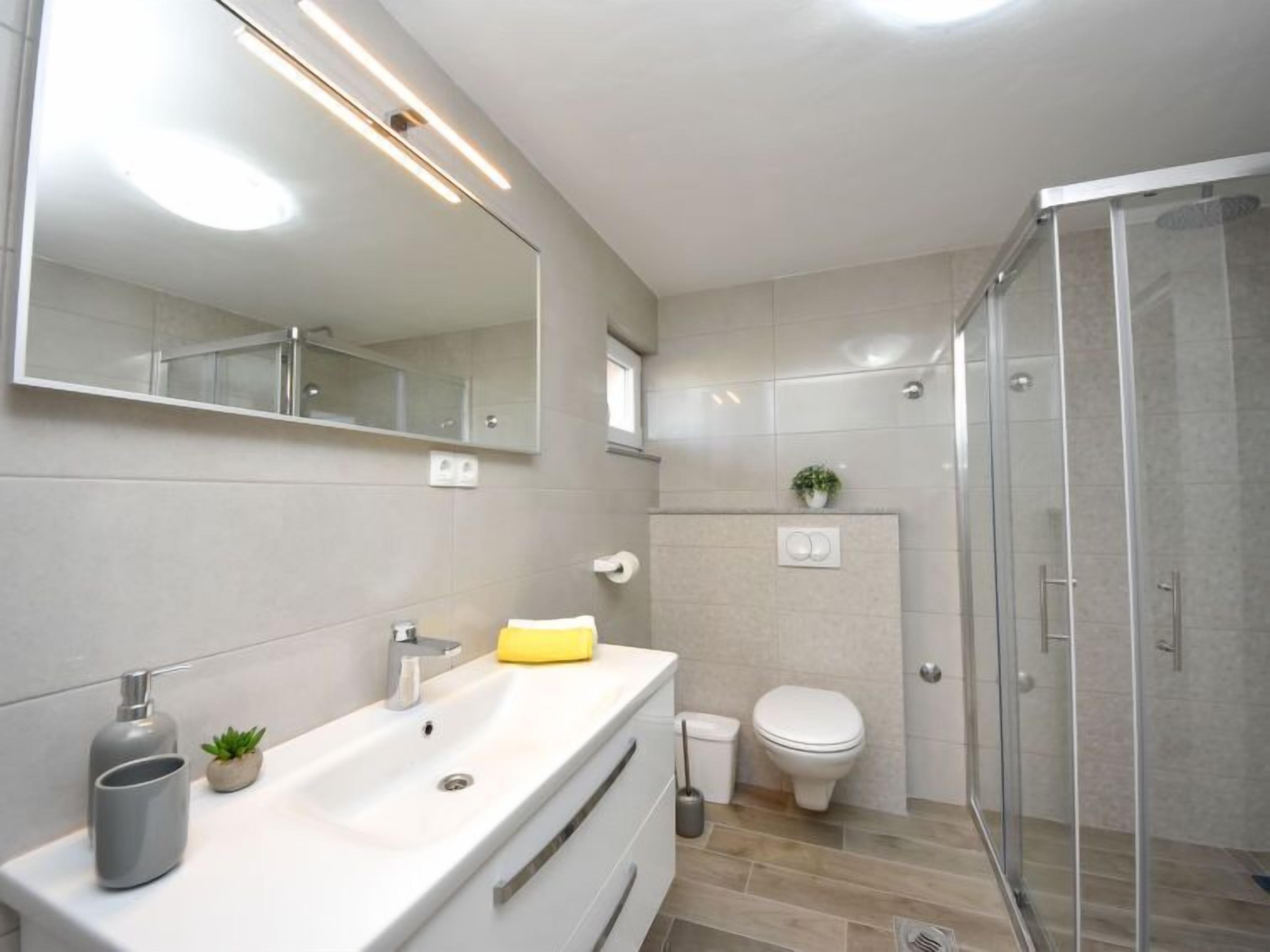 Et moderne badeværelse med et stort spejl, en vask, et toilet og en brusekabine i glas.