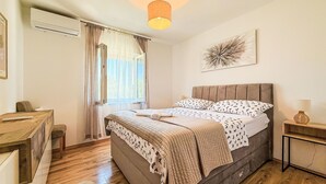 A bedroom with a bed, bedside table, lamp, and a window with curtains. - Tina & Tino by Interhome (Zadar)