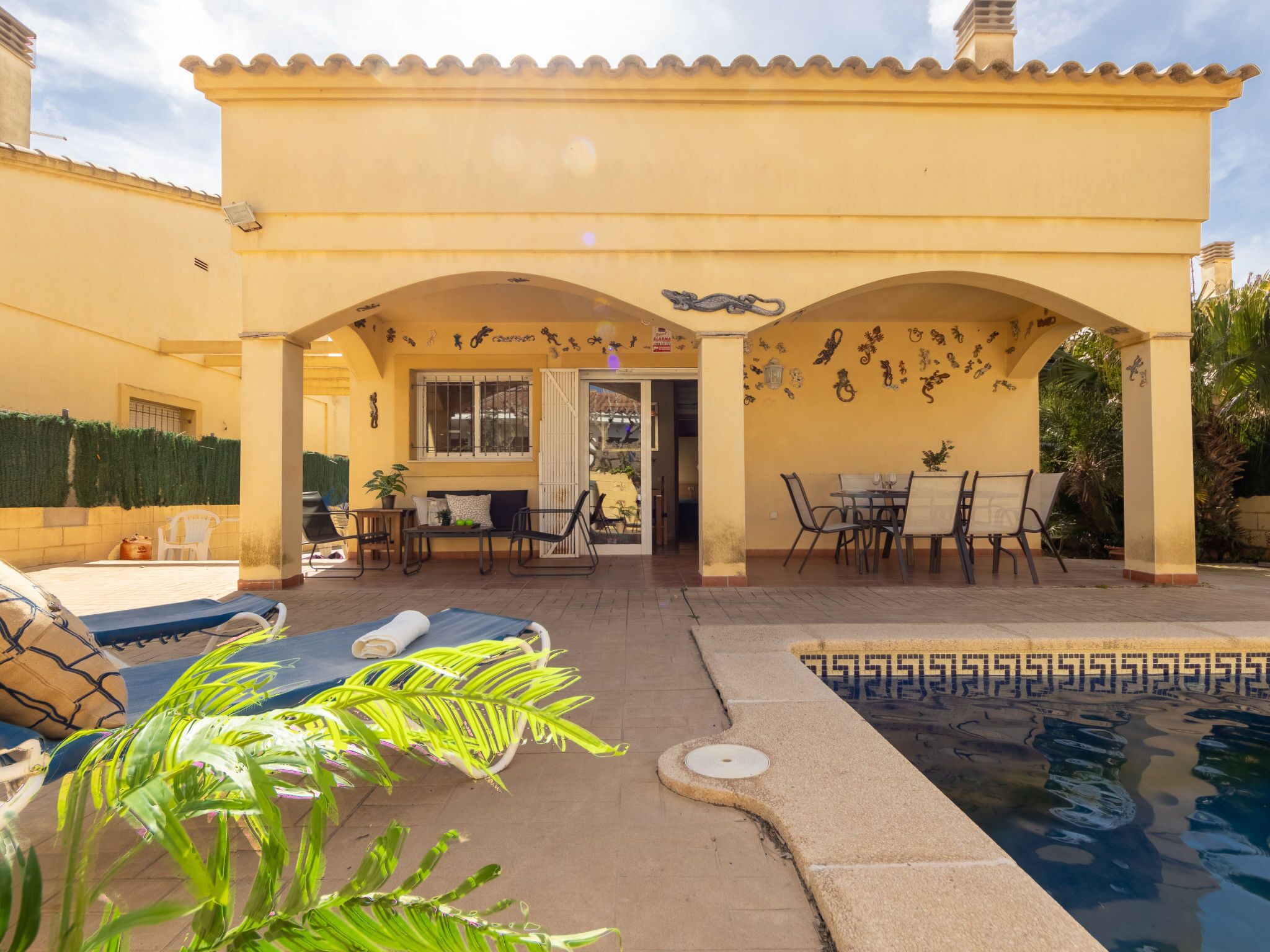 A covered patio area with a pool, outdoor seating, and decorative wall art.