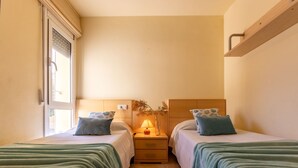 Een kleine, gezellige kamer met twee eenpersoonsbedden, een nachtkastje met een lamp en een raam met jaloezieën.