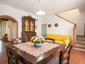 A dining area with a wooden table, chairs, a floral centerpiece, a cabinet, and a yellow sofa.