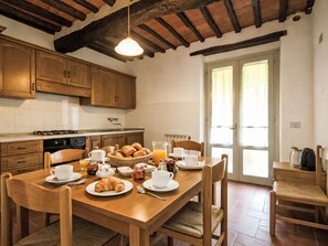 A wooden dining table with chairs, a kitchen area with wooden cabinets, a stove, and a window with curtains.