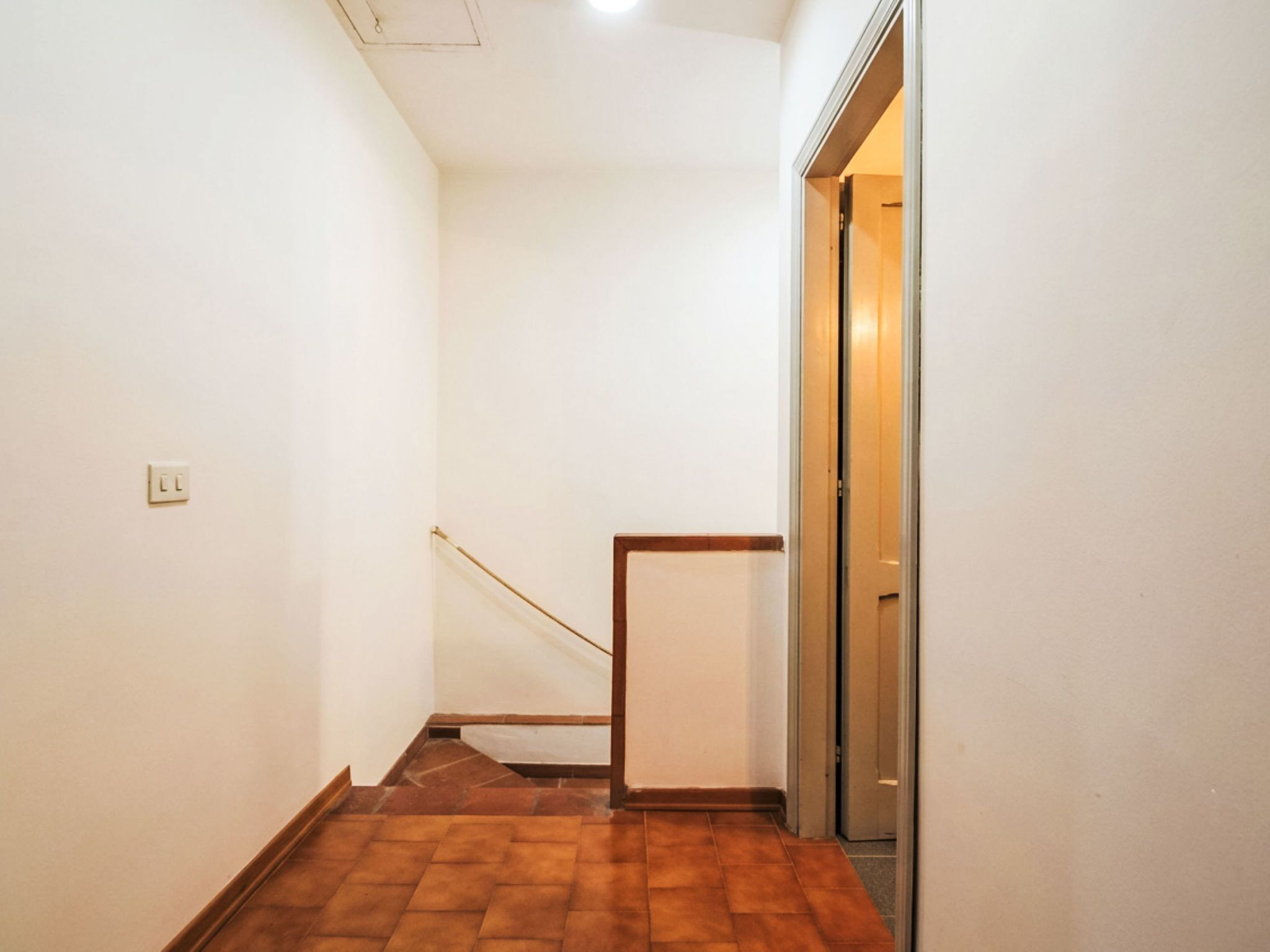 A narrow hallway with a wooden floor, a white wall, and a door at the end.