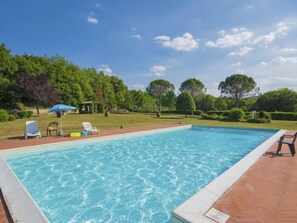 Una piscina rectangular amb una terrassa de fusta al voltant, un cobert i diverses gandules.