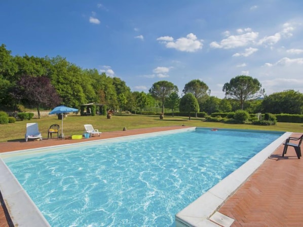 A rectangular swimming pool with a wooden deck surrounding it, a gazebo, and several lounge chairs.