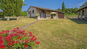 A house with a covered patio, a lawn, and a garden with red flowers. - Apartment Tegola by Interhome (Bucine)
