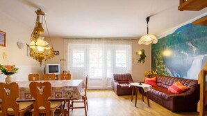 En hyggelig stue med spiseplads, møbler af træ, et stort muralmaleri og et fjernsyn.