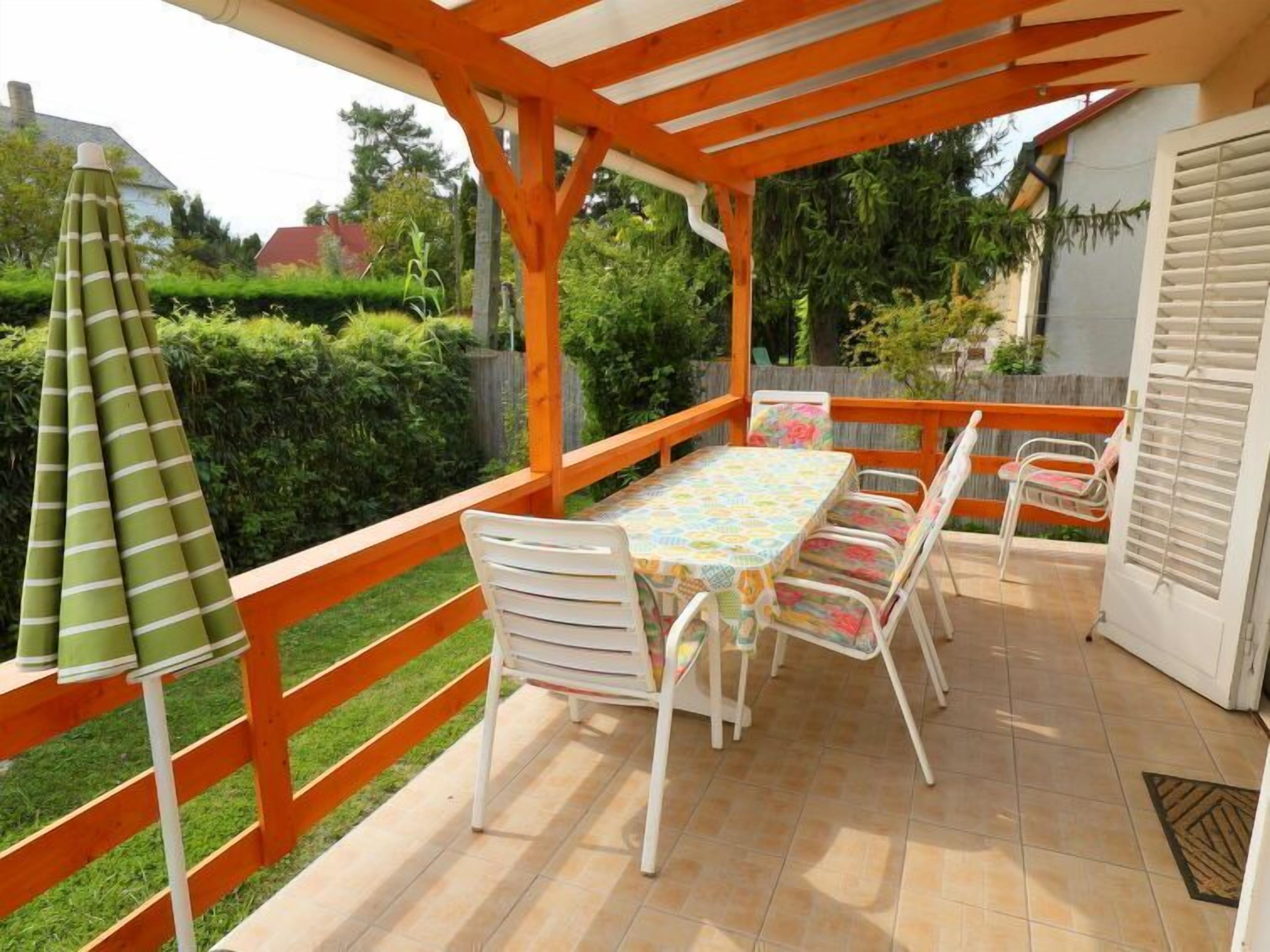 Une terrasse couverte, dotée d’une table et de chaises, entourée d’une clôture en bois et agrémentée d’un parasol vert.