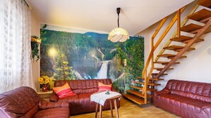 Ein Wohnzimmer mit einer Holztreppe, einer Sofagarnitur, einem Tisch und einem Wandgemälde eines Waldwasserfalls.