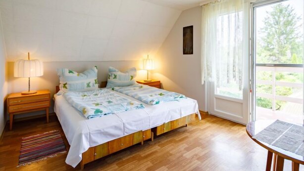 Ein Schlafzimmer mit einem Doppelbett, zwei Nachttischen mit Lampen, einem Holzboden und einem Fenster mit Vorhängen.