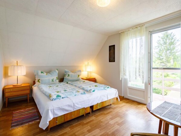 Une chambre à coucher avec un lit double, deux tables de chevet avec des lampes, un plancher en bois et une fenêtre avec des rideaux.