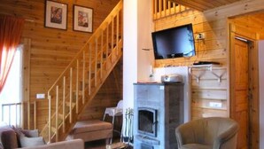 Ein Holzinnenraum mit Kamin, einem darüber montierten Fernseher, einer Treppe und einem Sofa.