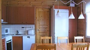 Eine kompakte Küche mit Holzausstattung, einer Mikrowelle, einem Spülbecken und einem kleinen Kühlschrank. Ein Holztisch mit vier Stühlen steht bereit.