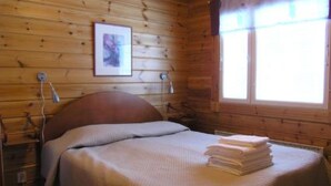 Ein Zimmer einer Holzhütte mit einem Bett, einem gerahmten Bild an der Wand und einem Fenster mit Vorhängen.