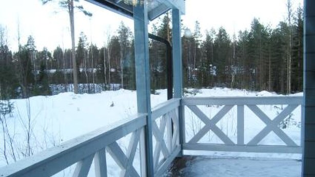Eine Holzterrasse mit weißer Brüstung, umgeben von schneebedecktem Boden und Bäumen.
