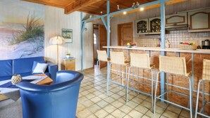 Un intérieur chaleureux avec un plafond en bois, un coin repas avec des chaises en métal et une cuisine dotée de meubles en bois.