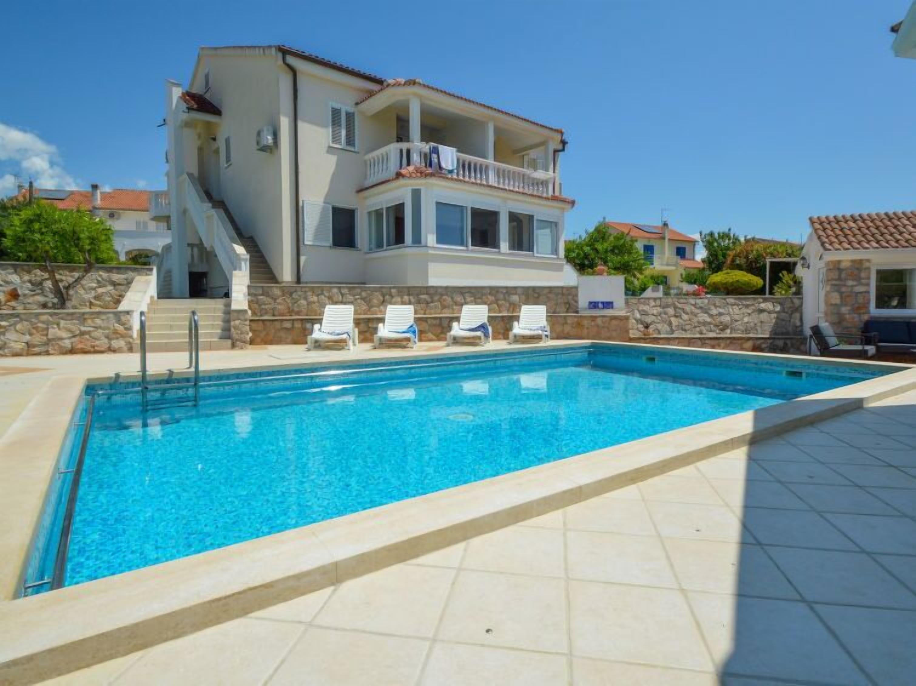 A swimming pool with four lounge chairs and a stone wall.